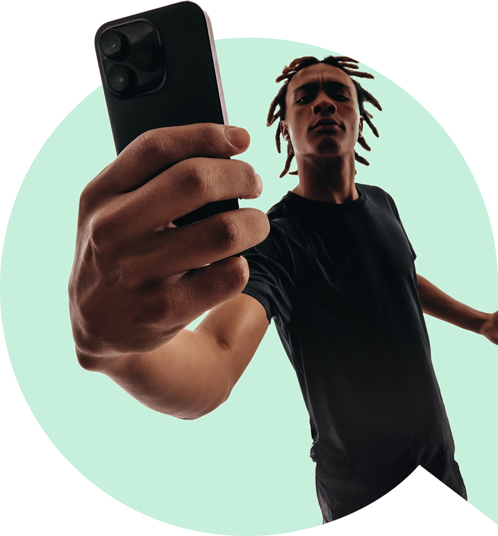 Young man holding a smartphone for a selfie in front of a green circular background