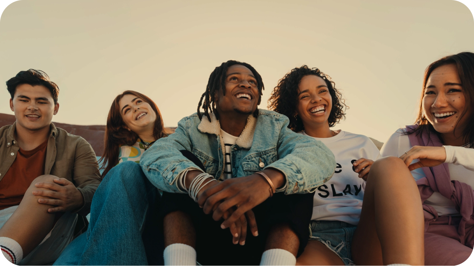 Five friends sitting together outdoors, smiling and laughing in the warm evening sunlight