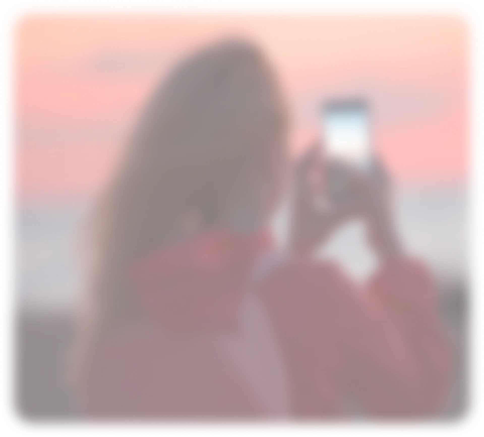 Woman in a red jacket taking a photo of the ocean at sunset with her smartphone